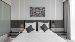 Un dormitorio moderno con una cama grande, dos mesitas de noche, un cabecero y una obra de arte colgada en la pared.