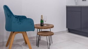 Una silla azul con patas de madera, una mesita de madera con una botella y un vaso, y un armario gris.