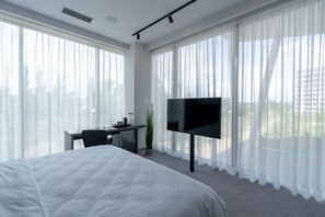 Una camera d'albergo moderna con un letto grande, una scrivania e una televisione a schermo piatto, oltre a tende leggere.