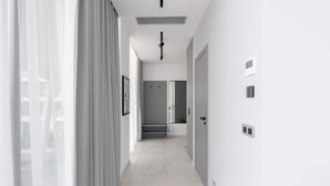 Un pasillo moderno y minimalista con paredes blancas, suelo de tonos claros y una puerta al final.