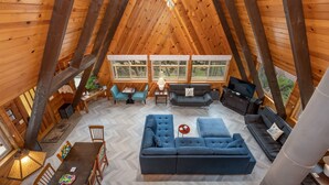 Un loft espacioso con techos altos, vigas de madera, un sofá grande, un televisor y un comedor con sillas y una mesa.