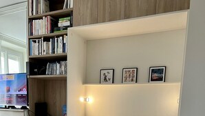 A neatly arranged bedroom with a bed, bedside tables, a bookshelf, and a TV on a stand. - Appartement Debourg Lyon 7 (Lyon)