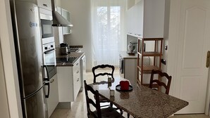 A compact kitchen with modern appliances, a dining table with chairs, and a view of a snowy landscape through the window. - Appartement Debourg Lyon 7 (Lyon)