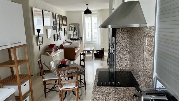 A modern kitchen with a built-in stove, granite countertops, and a dining area with a wooden table and chairs. - Appartement Debourg Lyon 7 (Lyon)