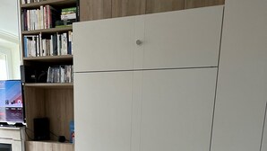 A room with a tiled floor, a white wardrobe, a wooden bookshelf, and a flat-screen TV displaying a time. - Appartement Debourg Lyon 7 (Lyon)
