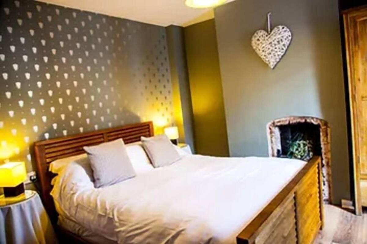 A bedroom with a bed, two bedside lamps, a heart-shaped wall decoration, and a wooden headboard.