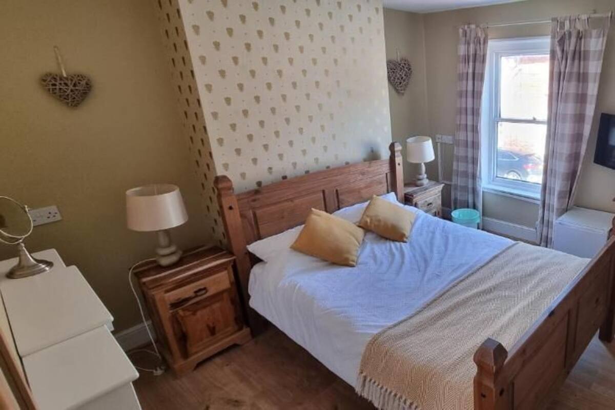 A bedroom with a wooden bed, bedside tables, a desk, a chair, a television, and a window with curtains.