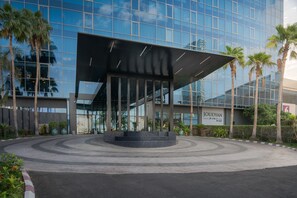 A modern building with a glass facade, palm trees, and a central plaza with a black structure. - Joudyan Jeddah Red Sea Mall (Jeddah)