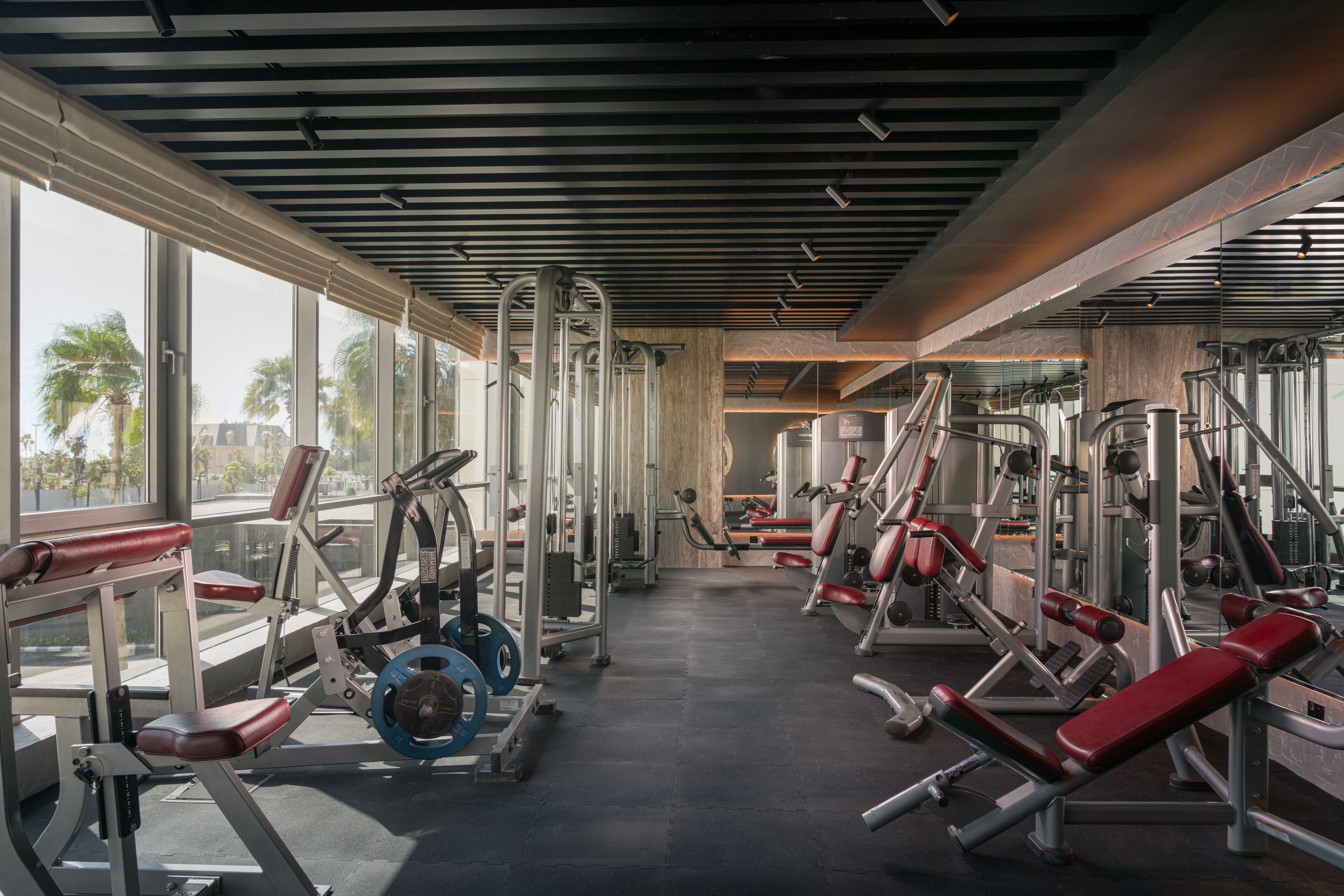 A gym with various exercise machines, large windows, and a modern ceiling design.