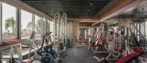 A gym with various exercise machines, large windows, and a modern ceiling design.