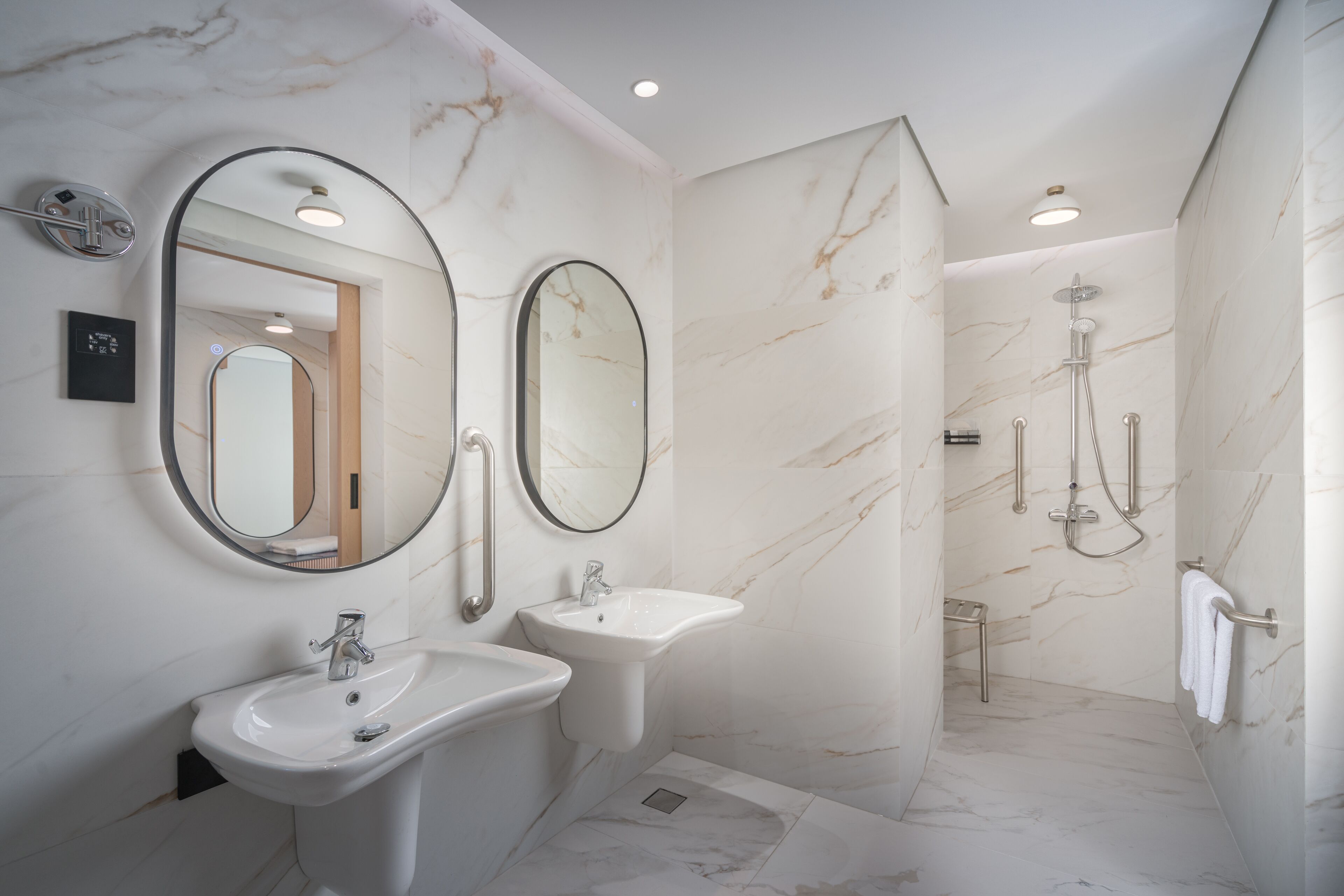 A modern bathroom with two sinks, two mirrors, and a shower area.