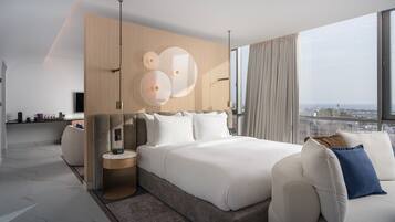 Habitación de hotel moderna con una cama grande, una mesita de noche y vistas a la ciudad a través de amplios ventanales.
