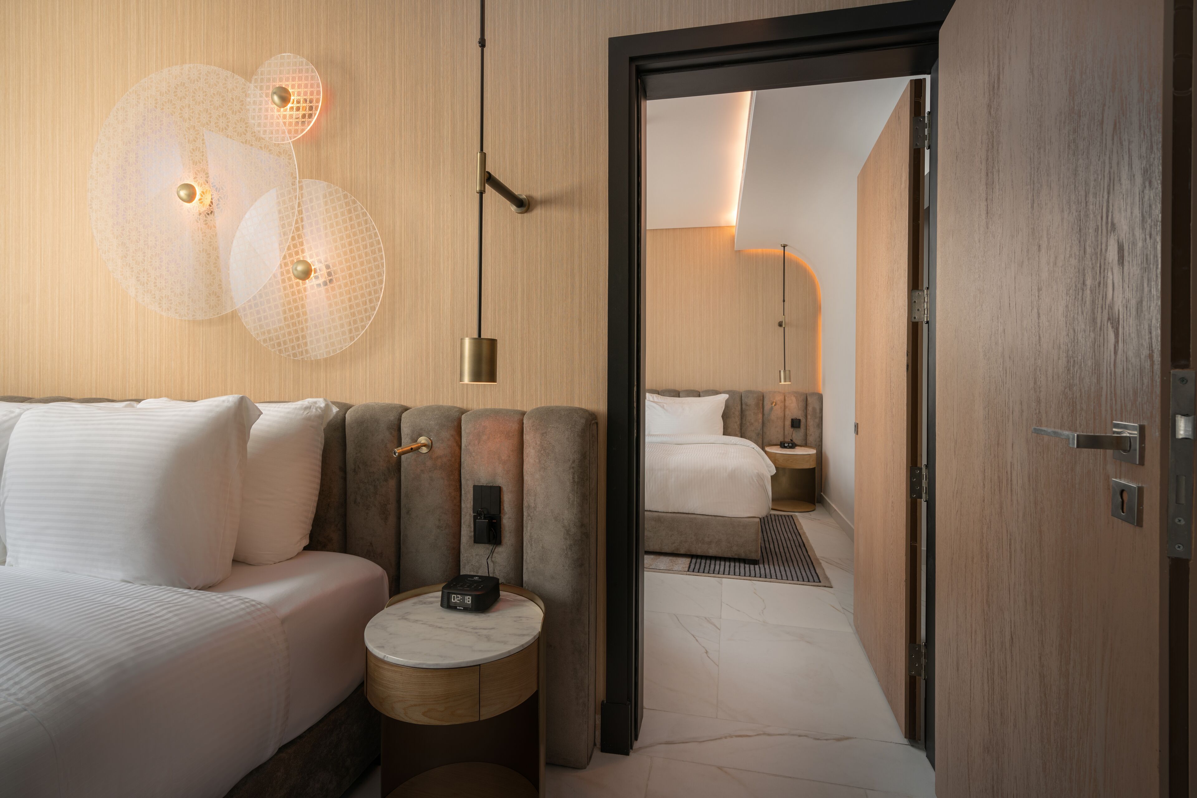 A modern hotel room with a large bed, a round side table, and a unique wall light fixture.