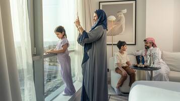 A hotel room with a large window, a bed, a sofa, and a small table with a tray of food.