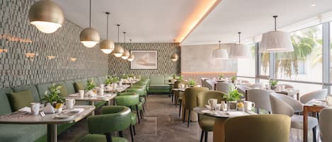 Ein modernes Restaurant mit grünen Sitzgelegenheiten, Pendelleuchten und einer Wand mit Muster.