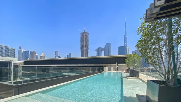 Une piscine sur le toit, avec la vue sur les toits de la ville en arrière-plan, dont un gratte-ciel particulièrement imposant.