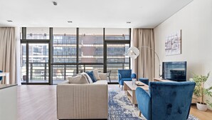 Un salon moderne avec un canapé, des fauteuils, un téléviseur et une grande fenêtre donnant sur la ville.