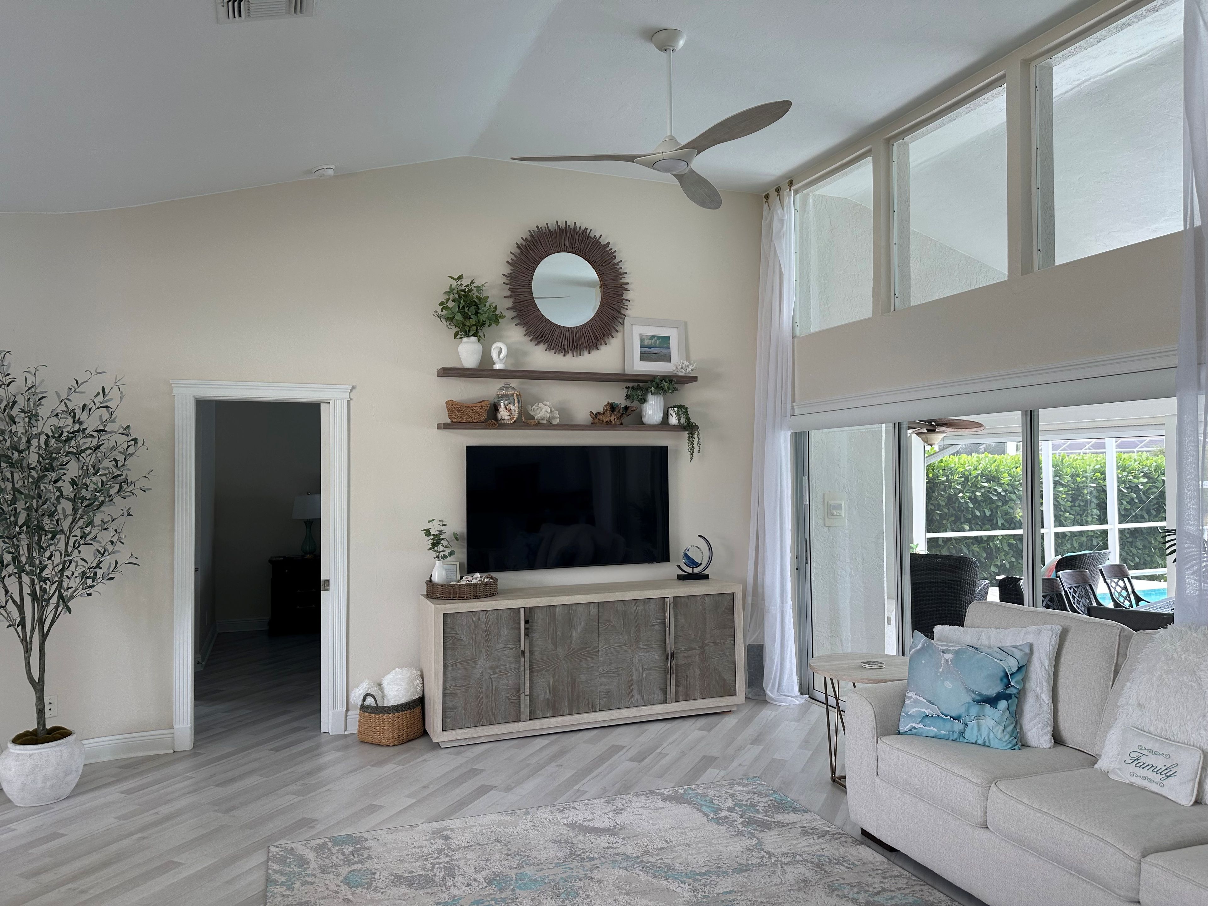 A living room with a television, ceiling fan, and large windows.