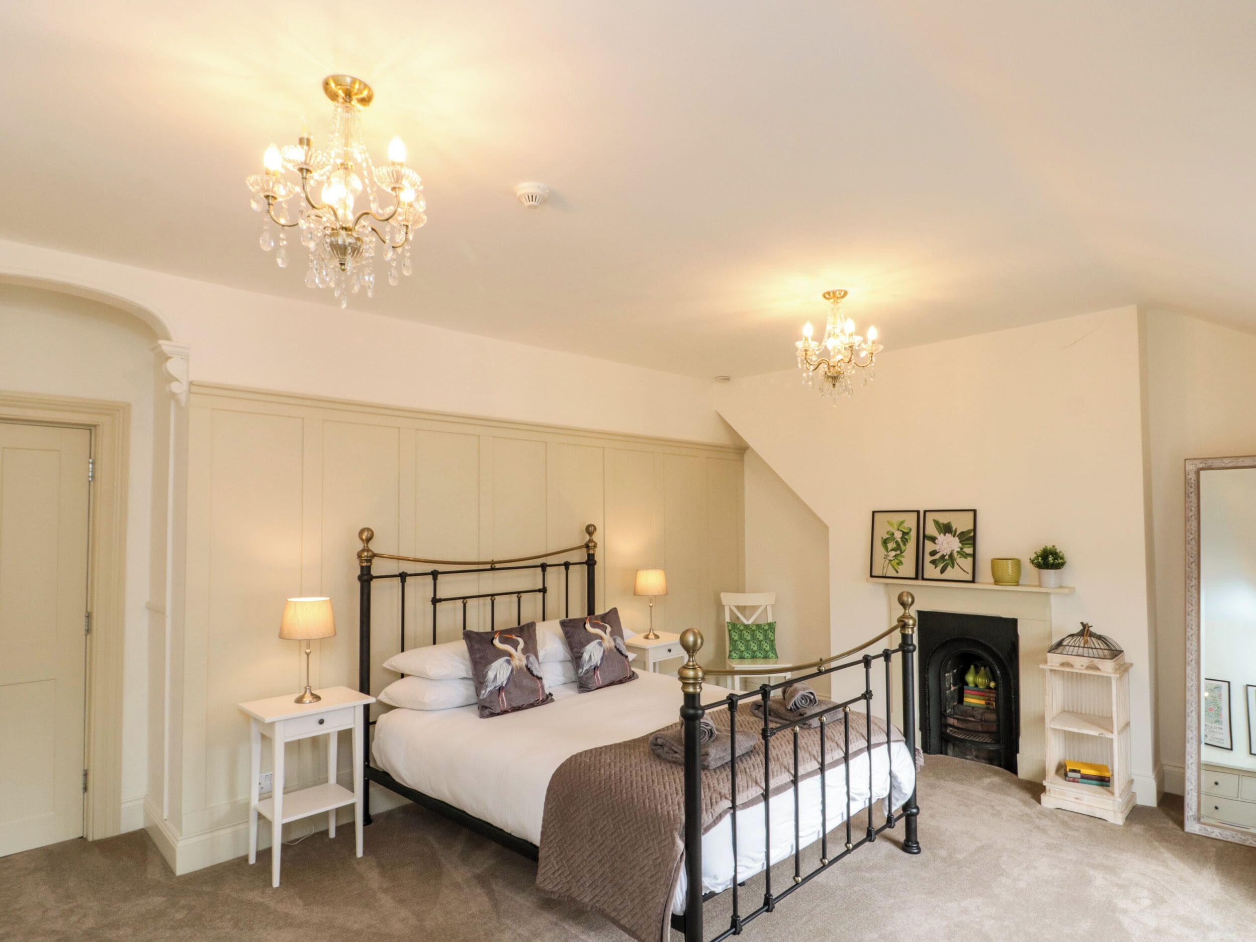 Une chambre à coucher avec un lit à baldaquin, un lustre, une table de chevet, une commode, une cheminée et une étagère avec des livres et des objets décoratifs.