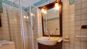 A bathroom with a glass-enclosed shower, a sink with a mirror above it, and tiled walls. - Studio Apartment B4 (Modena)