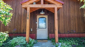 A wooden building with a number '150' on the door, a decorative glass door, and a wooden porch with a red roof. - Teton Homestead: Cozy Cabin in Downtown Victor (Victor)