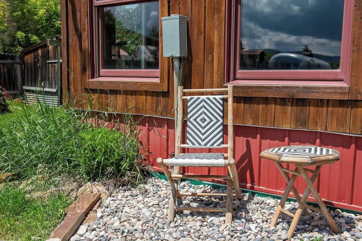 A wooden house with a red exterior, a wooden chair with a chevron pattern, and a small round table with a chevron pattern.