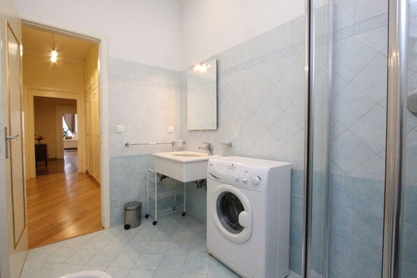 Een moderne badkamer met een wasmachine, wastafel en douche.