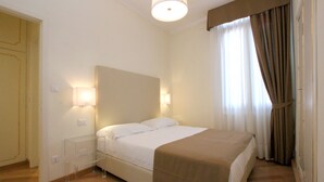 Una habitación de hotel con cama, lámparas de noche, suelo de madera y una ventana con cortinas.