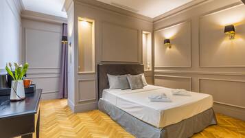 A neatly arranged bedroom with a bed, bedside lamps, a desk, and a potted plant.