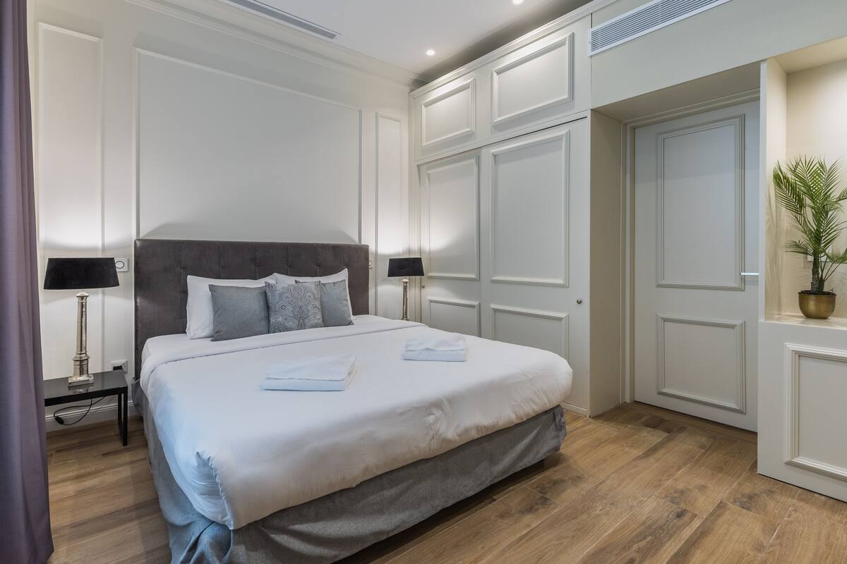 Un dormitorio ordenado con una cama grande, lámparas de noche y una planta en maceta.