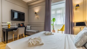 Habitación de hotel con cama, escritorio, silla, televisor y ventana con cortinas.