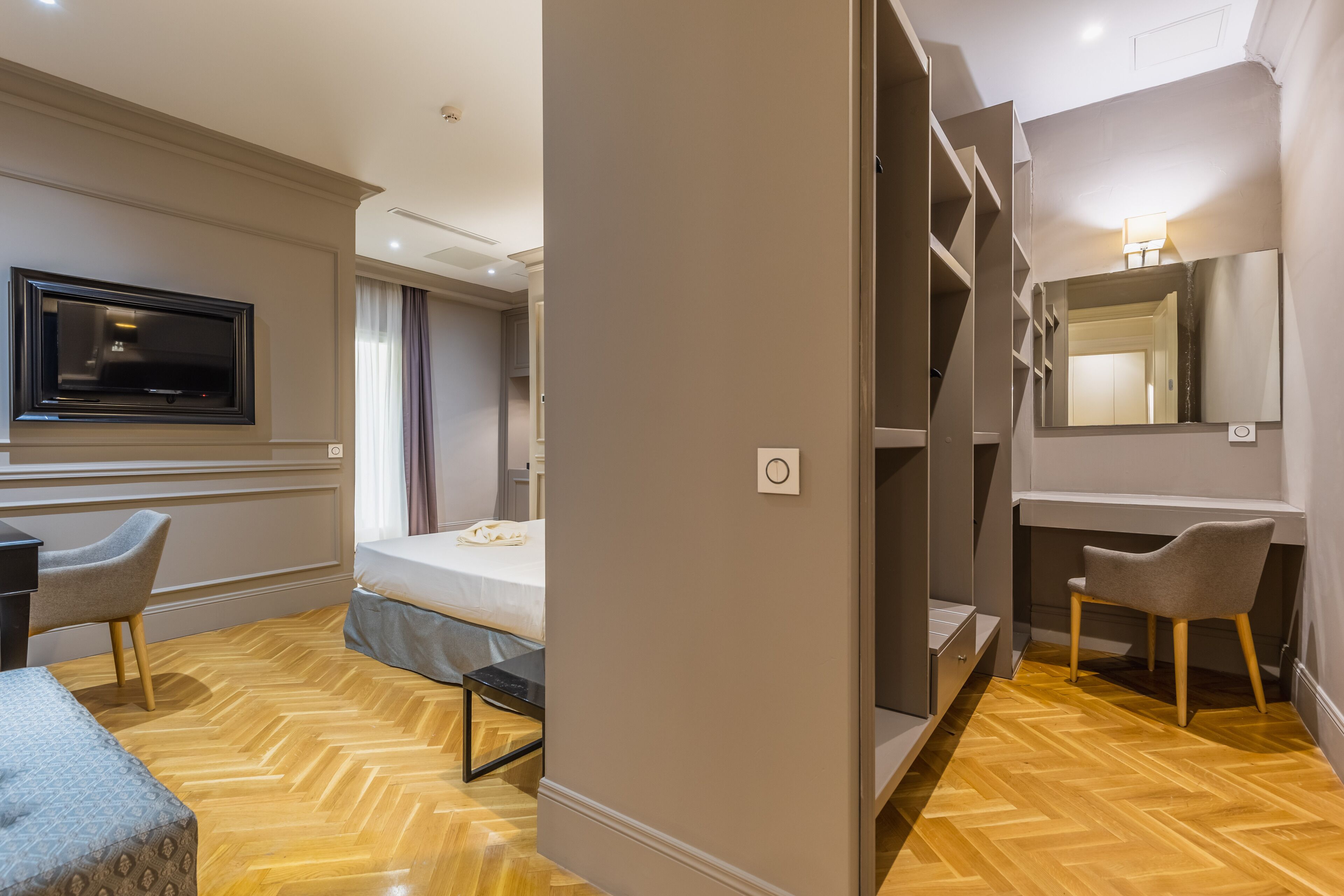 A hotel room with a bed, a desk, a chair, a TV, a mirror, and a wardrobe.