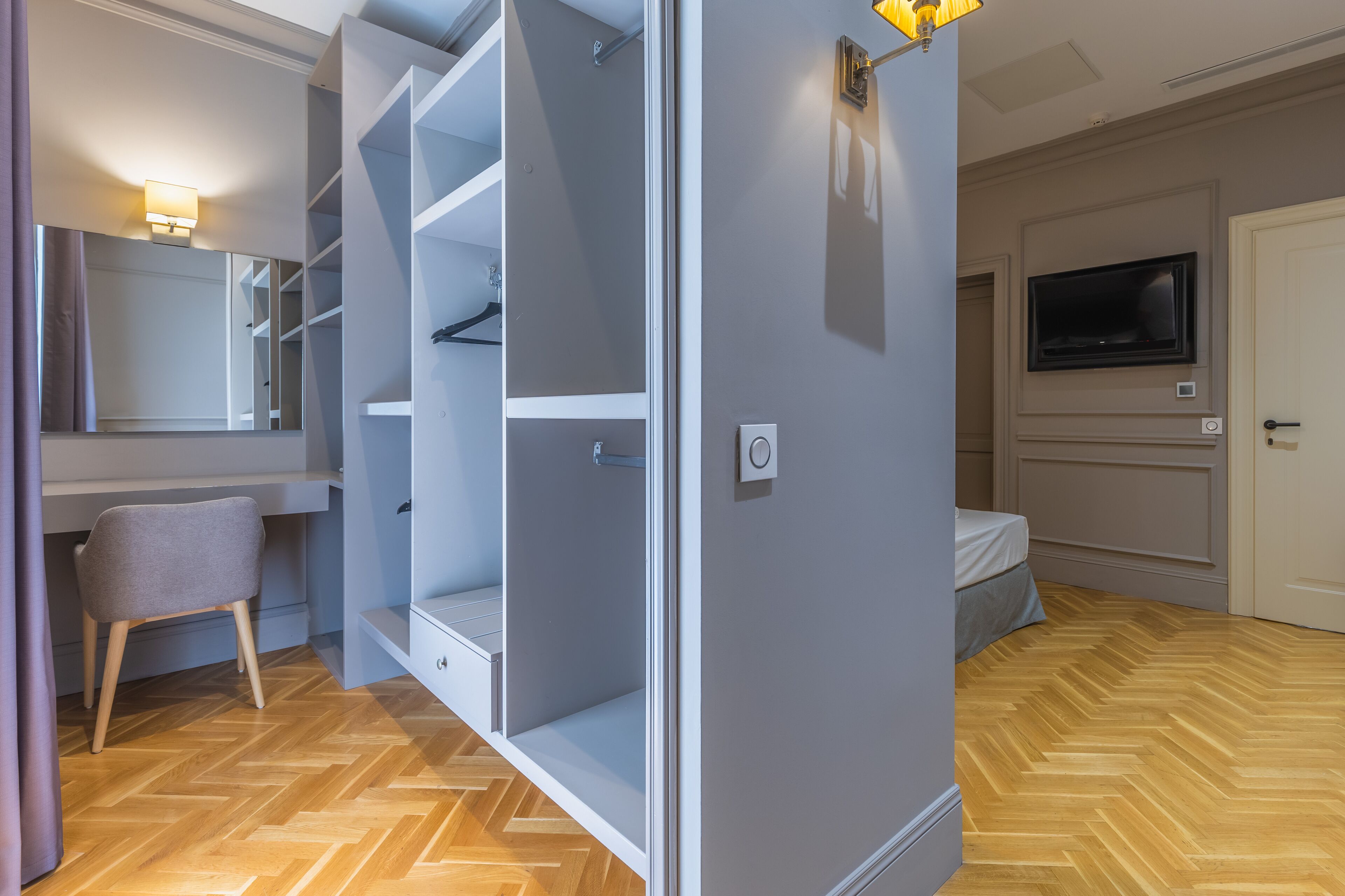 A modern bedroom with a built-in wardrobe, a flat-screen TV, and a herringbone-patterned wooden floor.