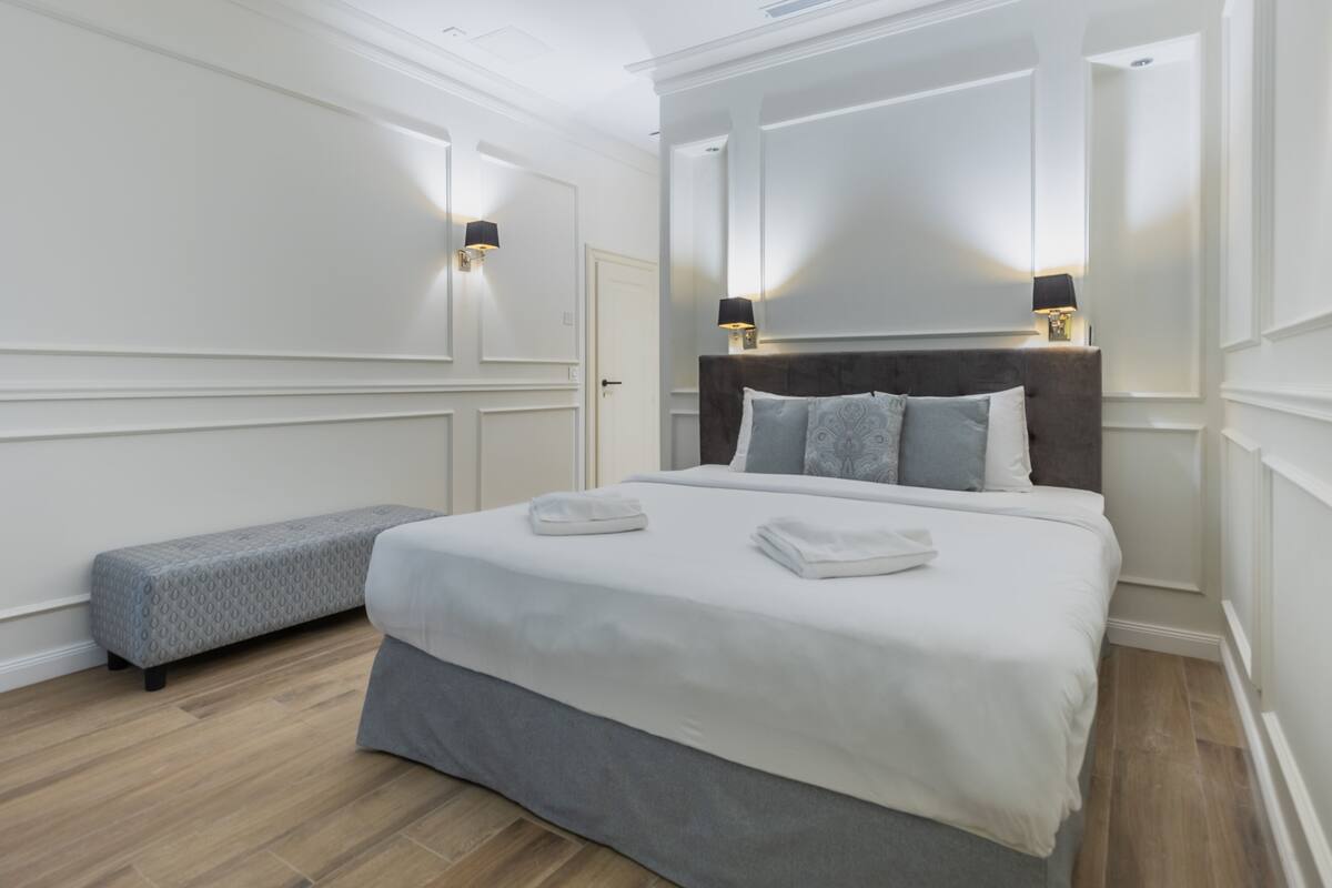 Un dormitorio ordenado con una cama grande, lámparas de noche y un banco.