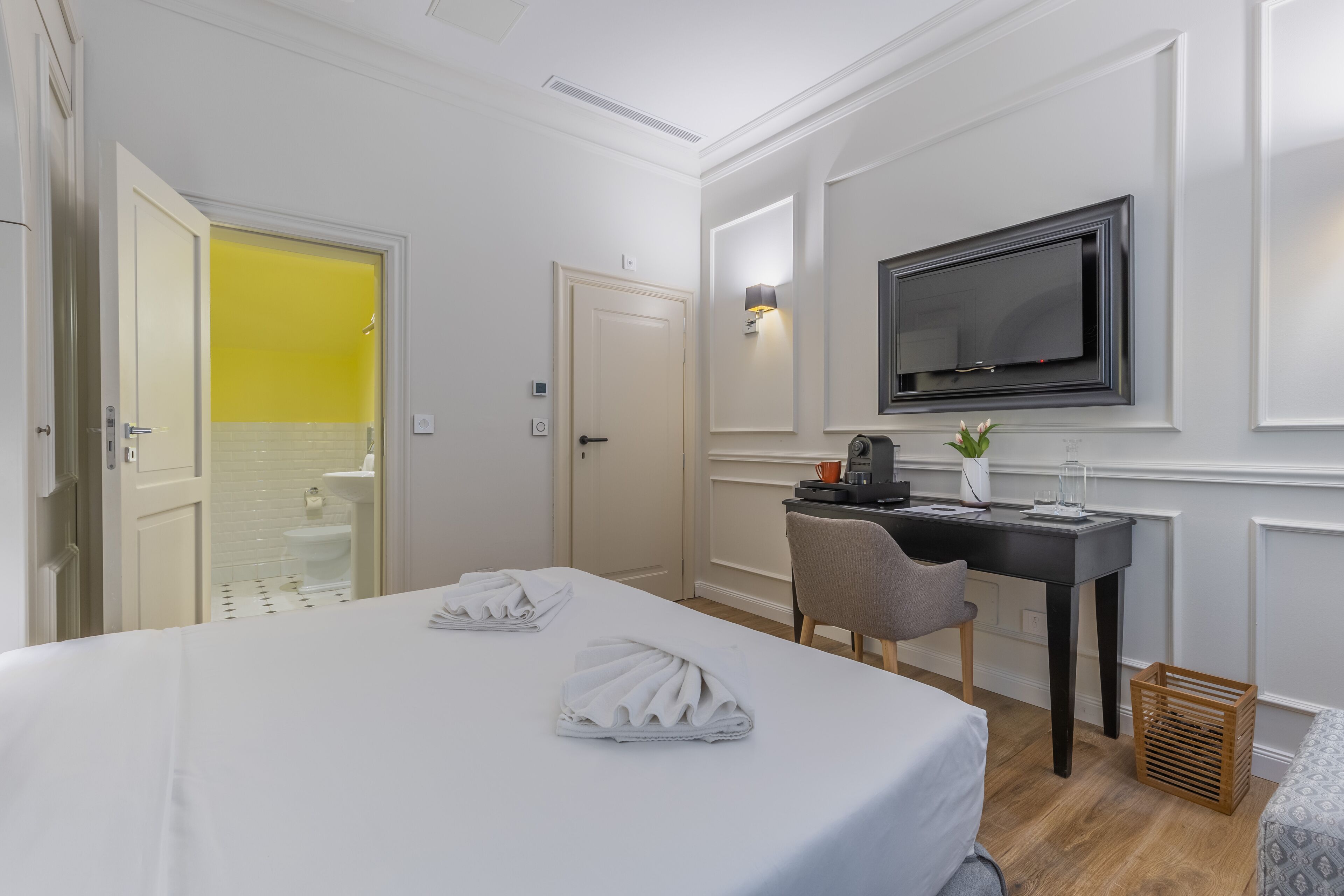 Une chambre d’hôtel avec un lit, un bureau, une chaise, une télévision et une petite plante.