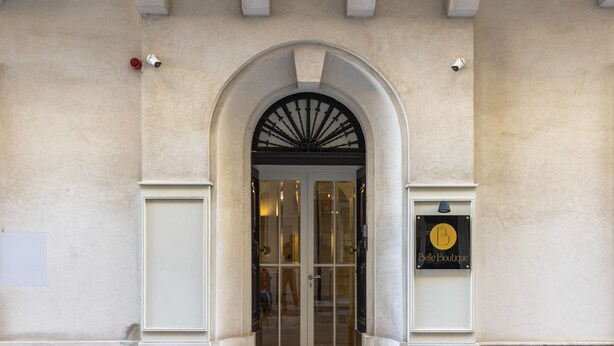 Una entrada arqueada con puerta de vidrio, un letrero con el logotipo 'B' y un escalón que lleva a la puerta.