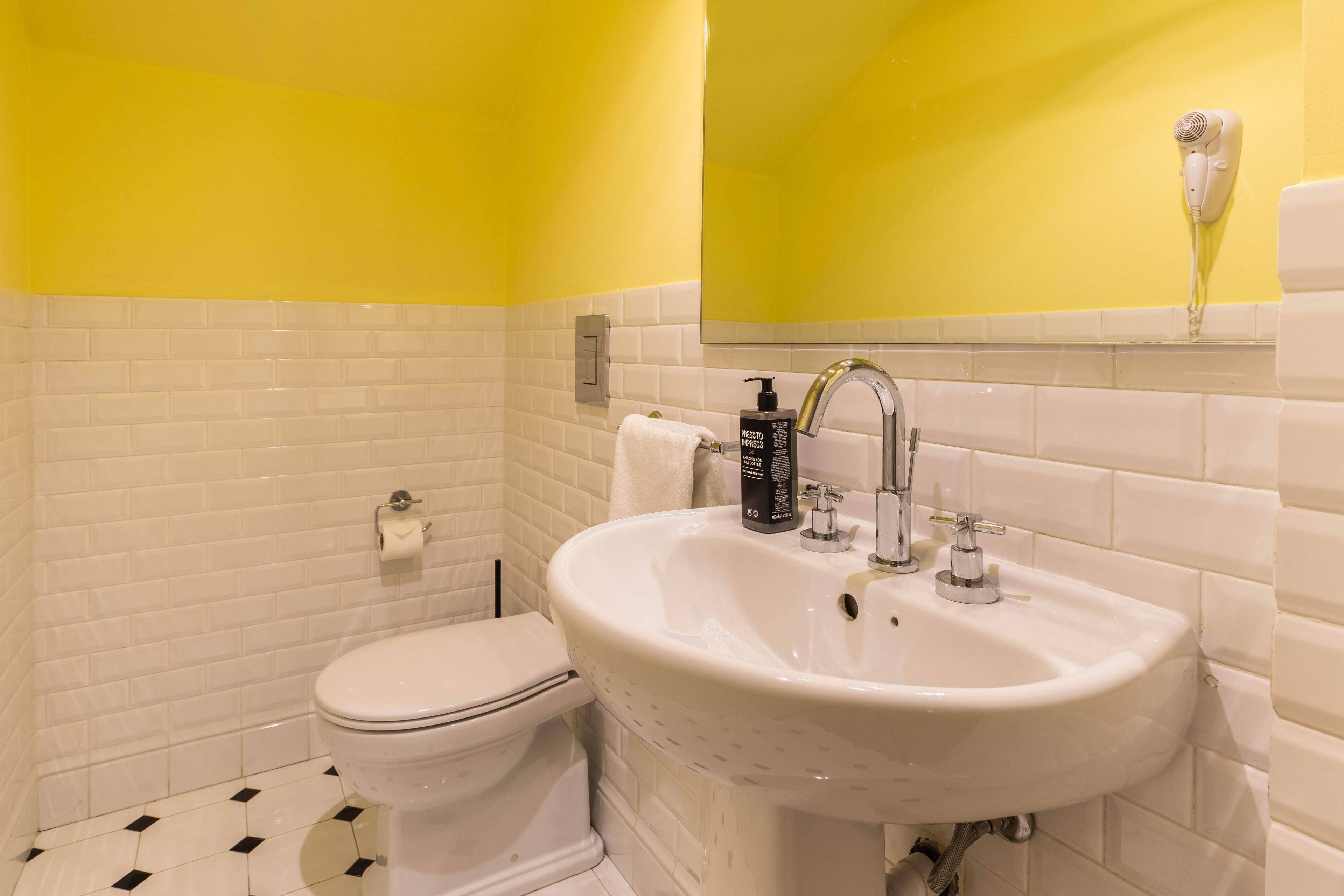Une salle de bain avec un lavabo blanc, des toilettes et un mur jaune.