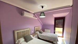 Une chambre avec deux lits simples, un ventilateur de plafond et une fenêtre avec des stores.