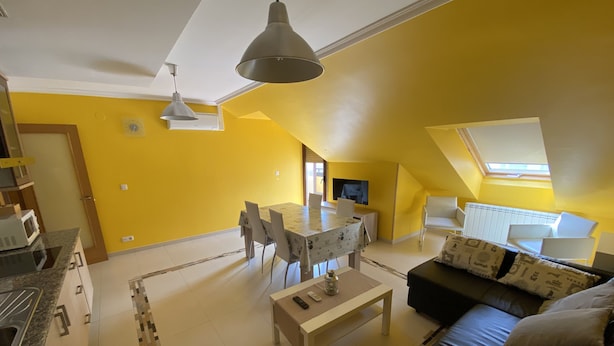 Une pièce lumineuse aux murs jaune vif, comprenant une table à manger, des chaises, un canapé et un téléviseur.