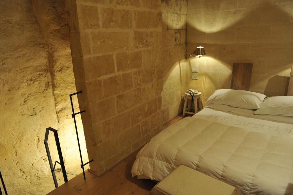 Ein Schlafzimmer mit Steinsandsteinwand, einem Bett mit weißer Bettwäsche, einem Nachttisch und einer Wandleuchte.
