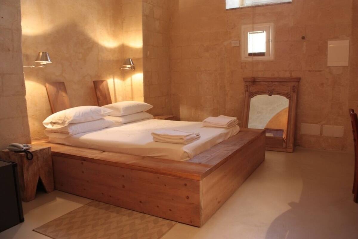 A wooden bed with white linens, two wall-mounted lamps, and a small mirror above the bed.