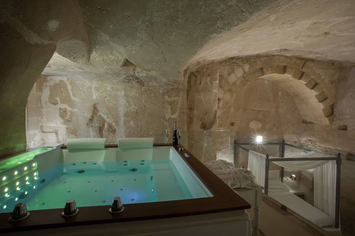 A spa room with a large bathtub, a glass enclosure, and a bed with white linens.