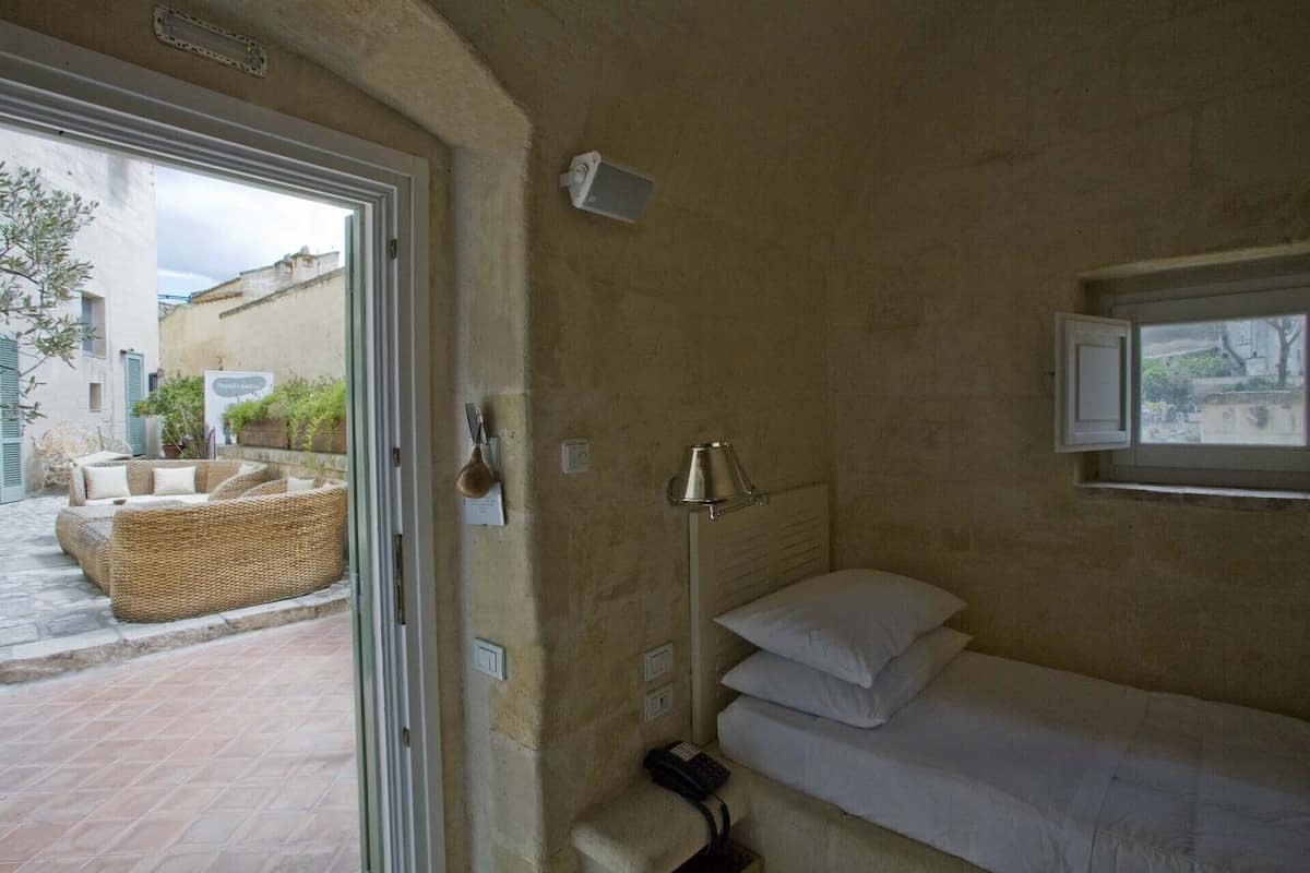 A small, cozy room with a bed, a bedside lamp, and a window.
