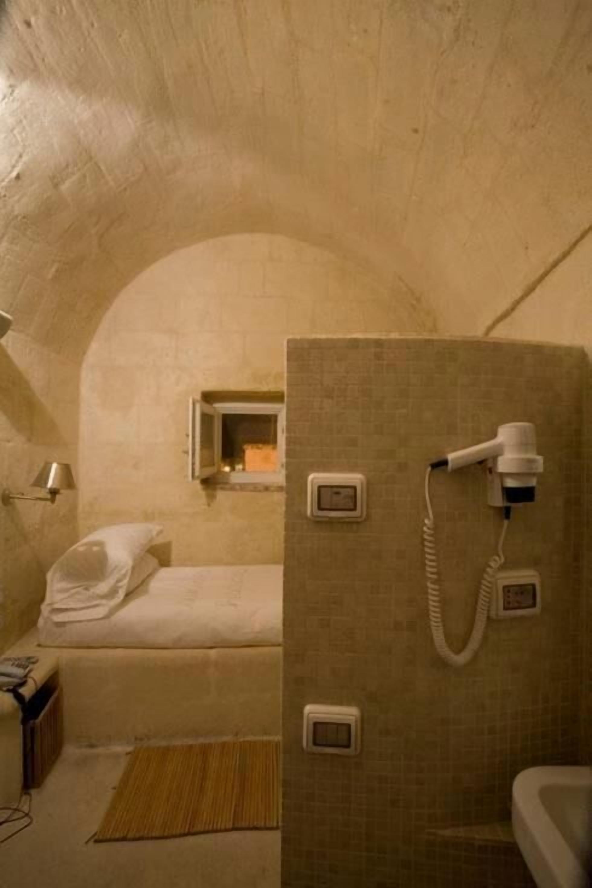 A small, dimly lit room with a single bed, a portable heater, and a portable toilet.