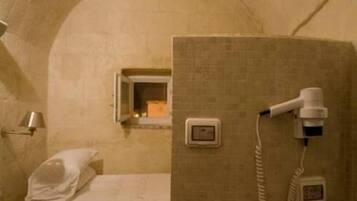 A small, dimly lit room with a single bed, a portable heater, and a portable toilet.