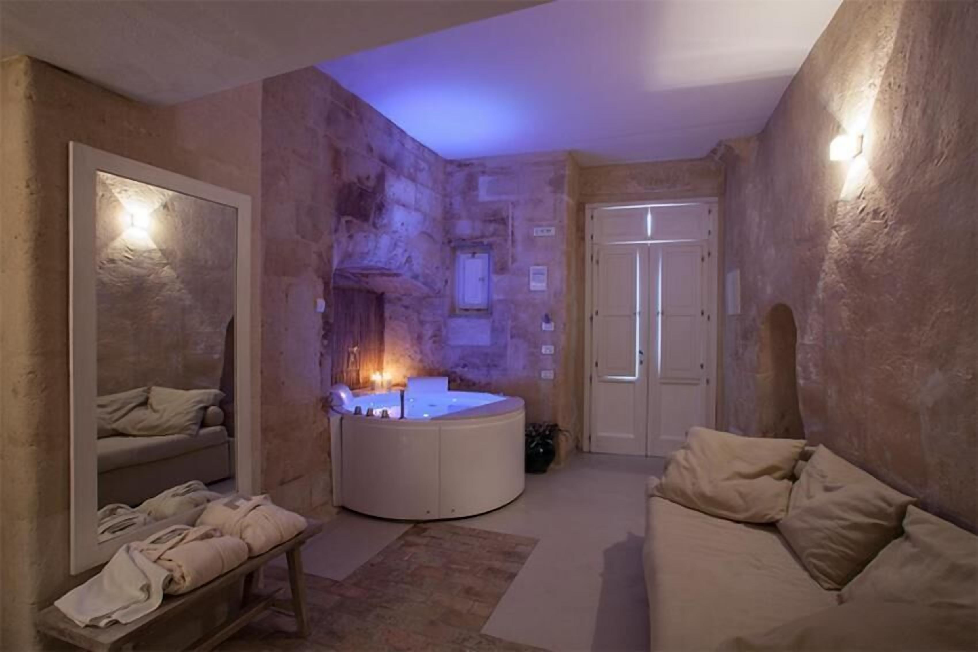 A spa room with a stone wall, a massage table, a massage chair, and a bathtub.