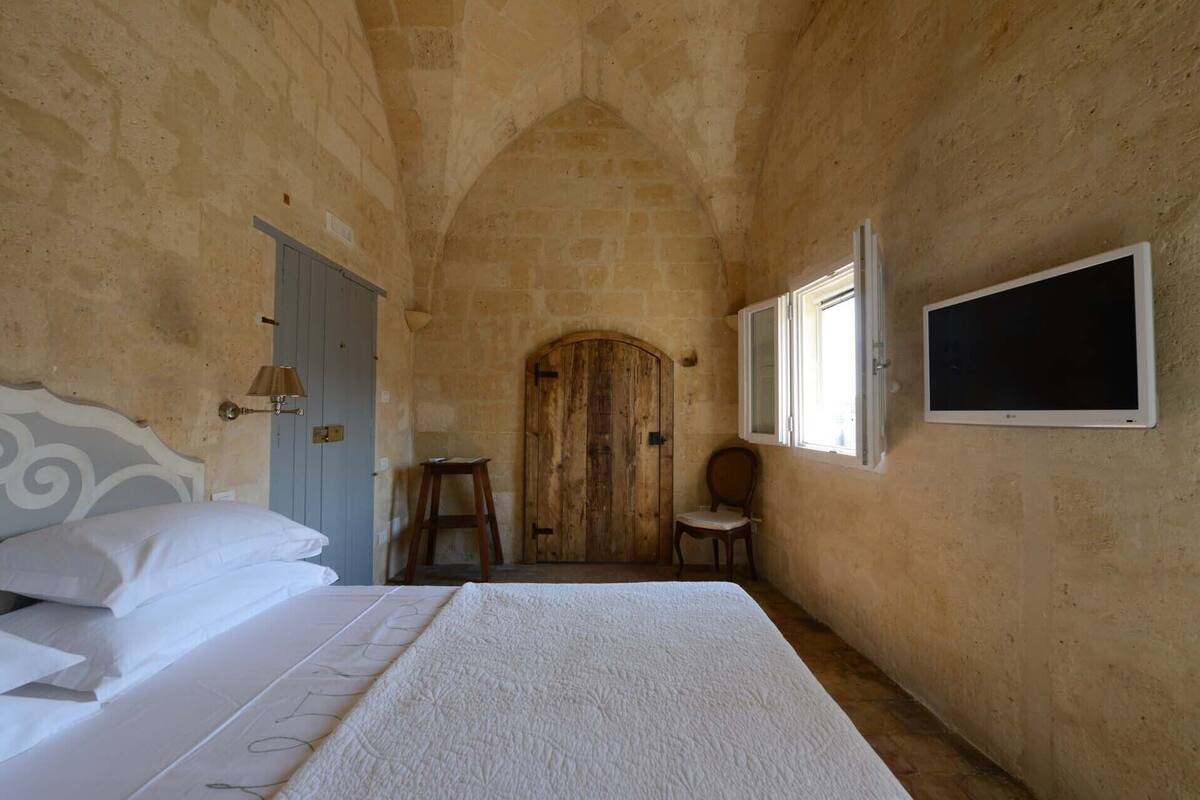 A bedroom with a bed, a wooden door, a chair, and a TV mounted on the wall.