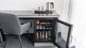 Eine kleine Küchenzeile mit einem Kühlschrank, einer Kaffeemaschine und einem Glas Wasser auf der Arbeitsfläche.