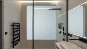Ein modernes Badezimmer mit Duschkabine aus Glas, einem schwarzen Handtuchhalter und einem großen Spiegel.