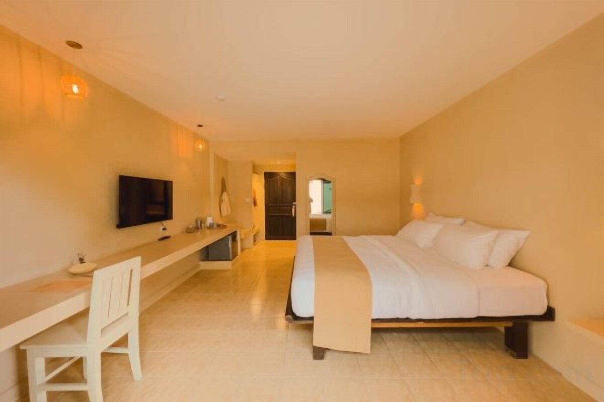 A hotel room with a bed, a desk, a chair, a television, and a bathroom visible in the background.